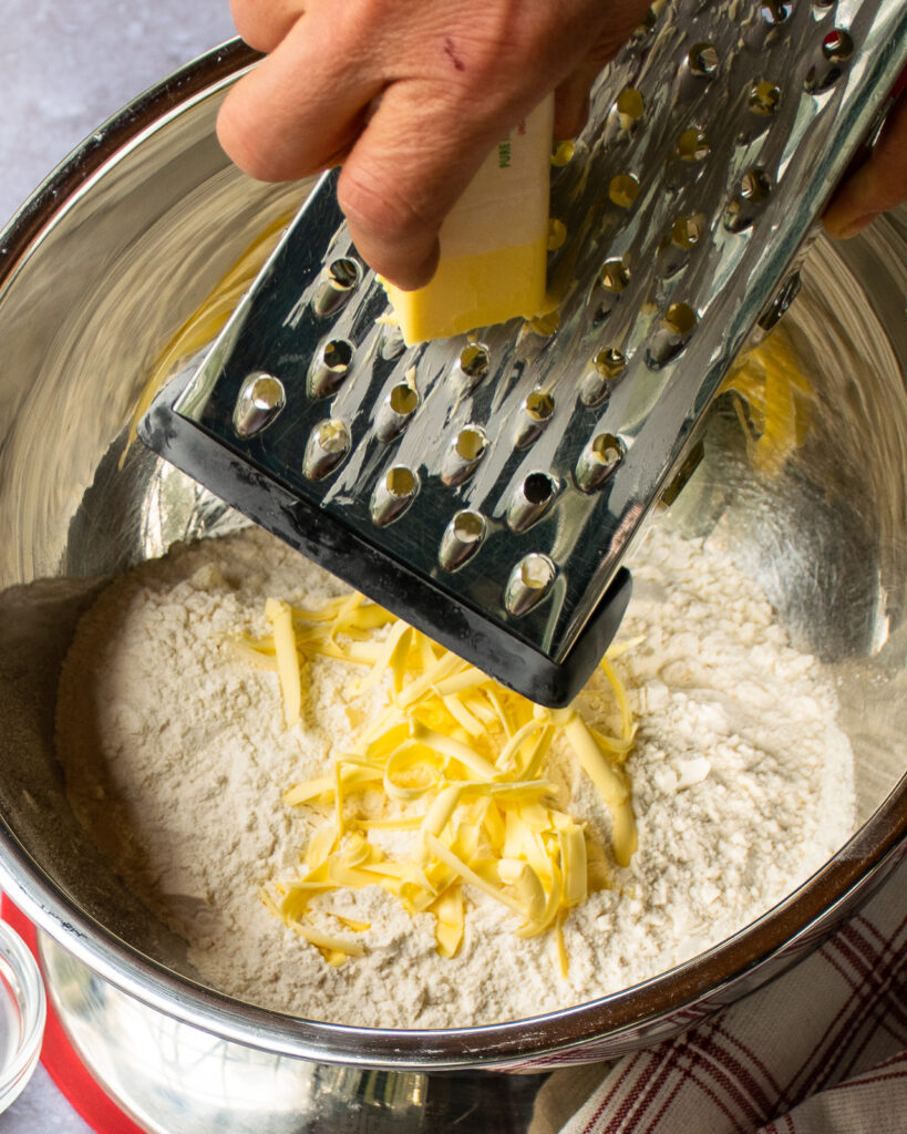 Hands grating butter into a bowl of dry ingredients.