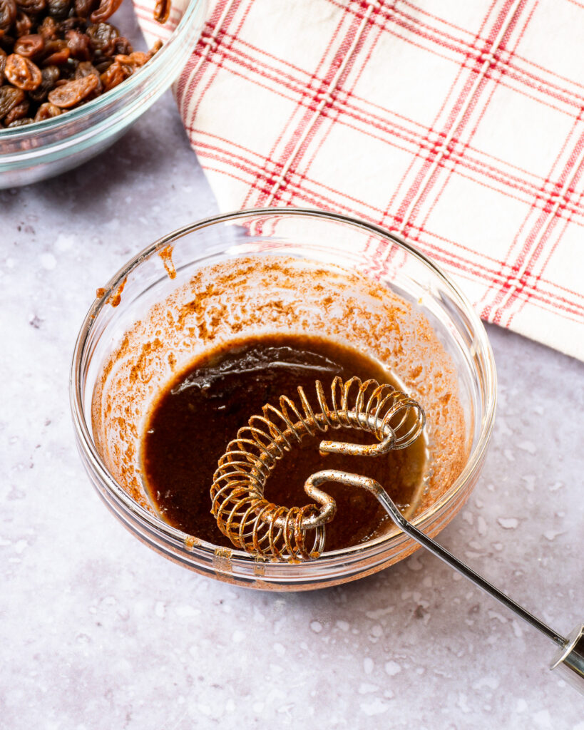 A bowl of cinnamon, brown sugar and butter with a whisk.