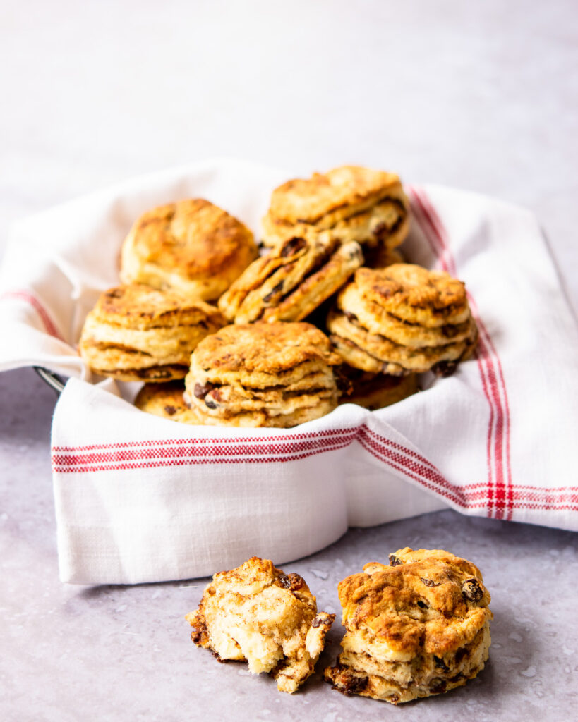 A basket of cinnamon raisin biscuits with one broken on the counter in front.