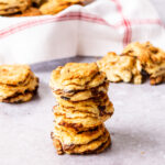 Three cinnamon raisin biscuits in a stack in front of a basket of more biscuits.