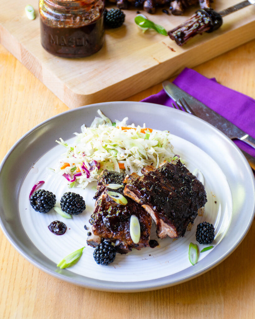 A plate with baby back ribs and coleslaw, with a purple napkin.