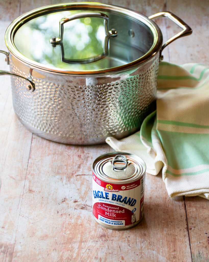 A can of sweetened condensed milk in front of a hammered stainless steel stockpot.