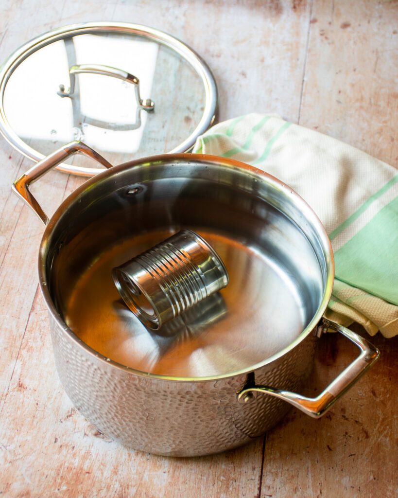 A can of condensed milk submerged in water in a stainless steel stockpot.