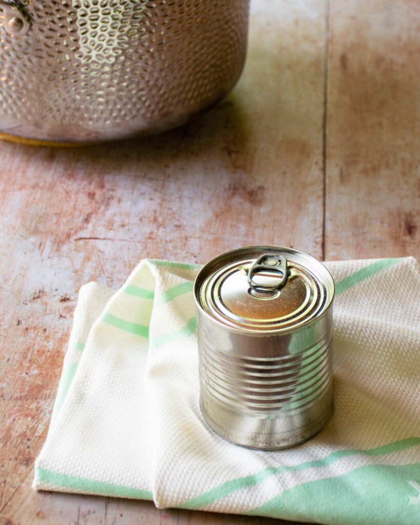 An unopened can of condensed milk on a towel with a stockpot in the background.