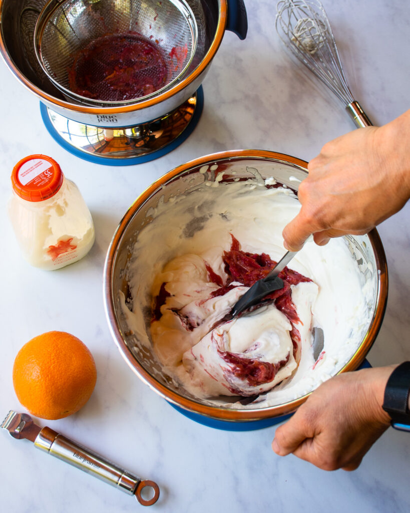 Hands folding stewed rhubarb into whipped cream.