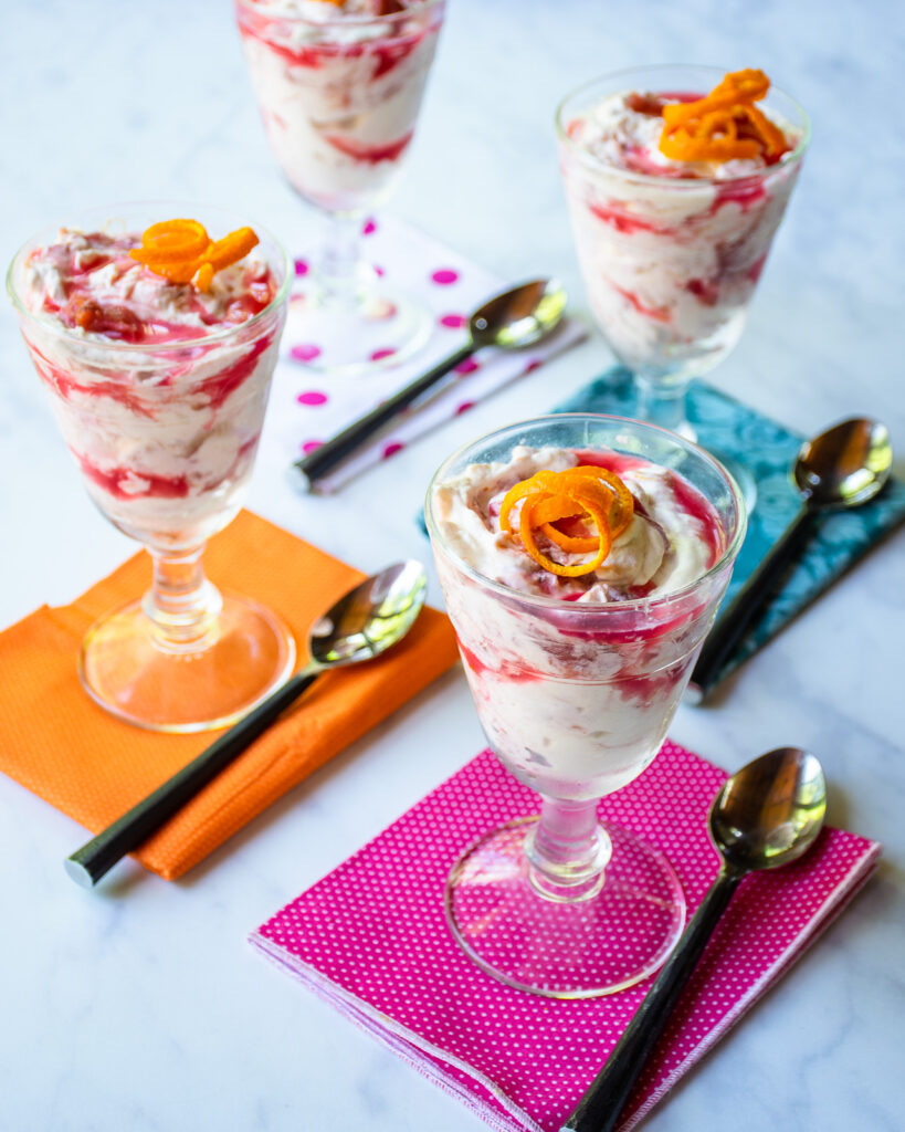 Four parfait glasses with rhubarb fool, four colorful napkins and four spoons on a table.