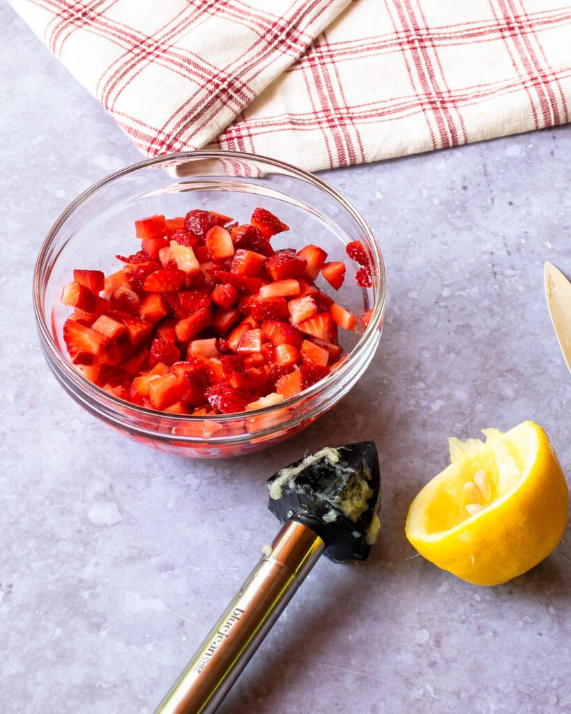 A bowl of diced strawberries with a half lemon and reamer next to it.