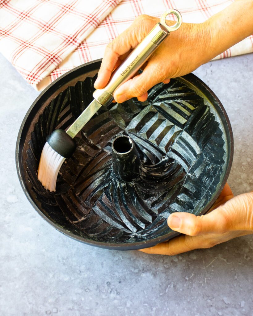 Hands brushing butter on the inside of a bundt pan with a basting brush.