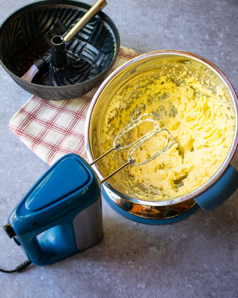 Butter and sugar creamed in a stainless steel bowl with a blue hand mixer next to it.