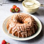 A strawberry pound cake in a bundt shape on a white plate with powdered sugar in the background.