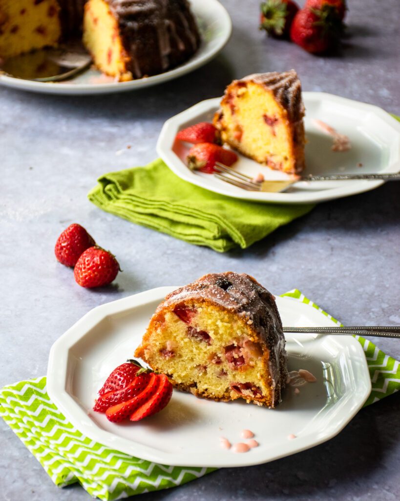 Two pieces of strawberry pound cake on white plates with green napkins and the rest of the cake in the background.