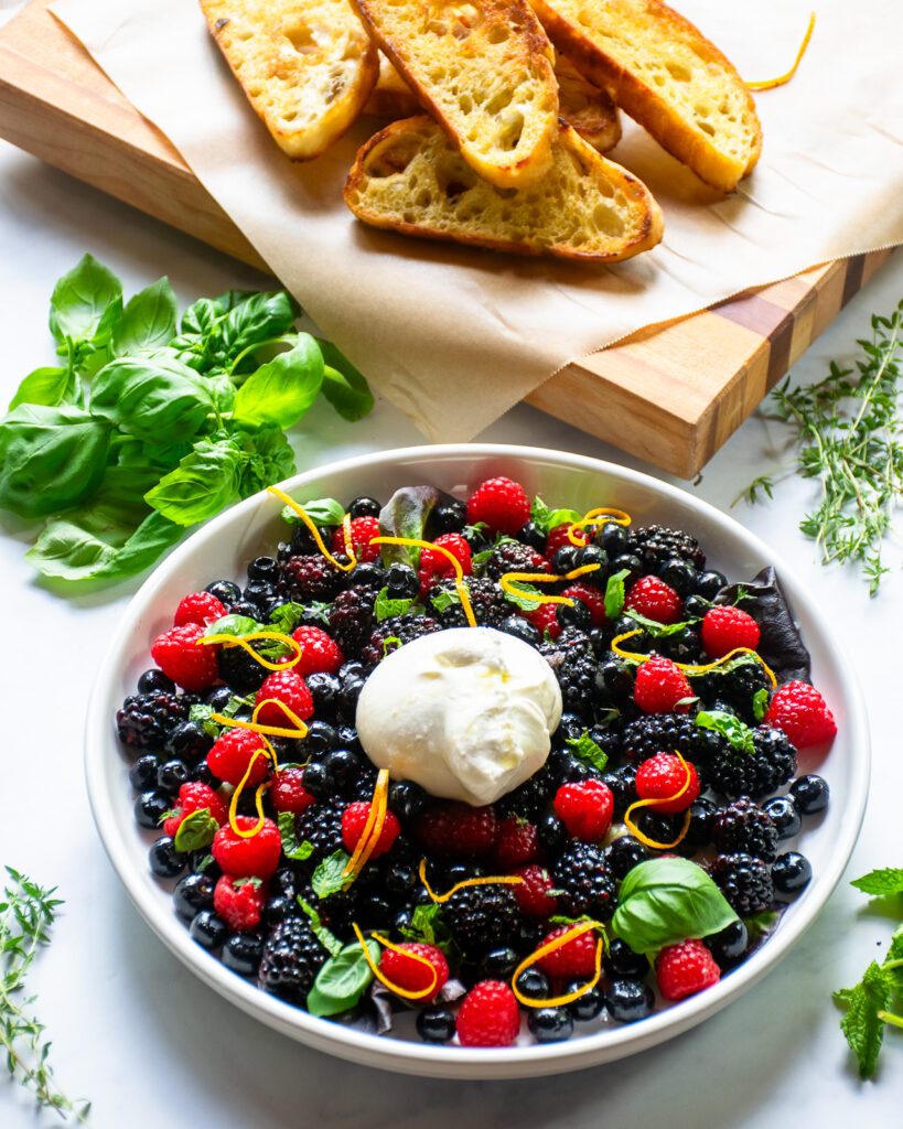 A plate of burrata and berry appetizer with fried ciabatta in the background.