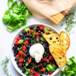 Looking down on a white plate with burrata and berry appetizer with some fried ciabatta on the side.