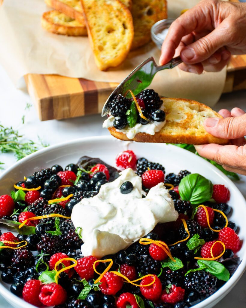 Spreading berries and burrata on a crostini.