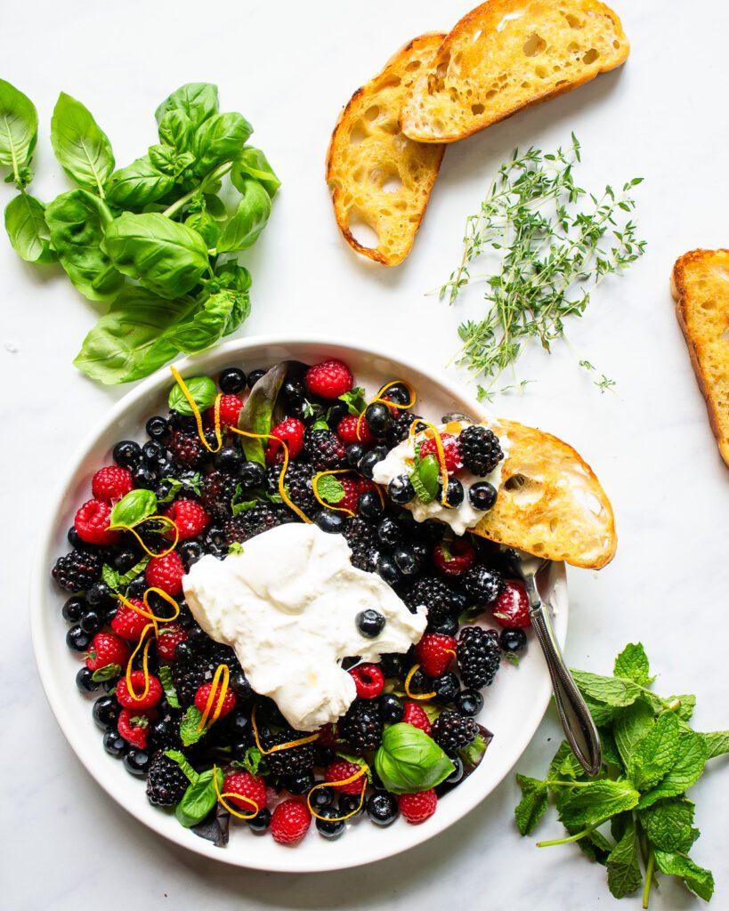 Looking down on a plate of burrata and berry appetizer with a crostini built on the side of the plate.