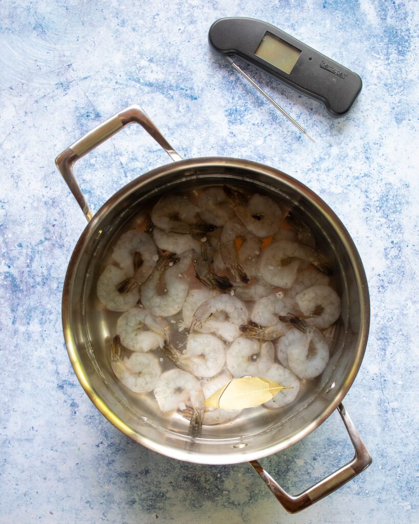 Raw shrimp in a saucepan of cold water with a digital thermometer next to it.