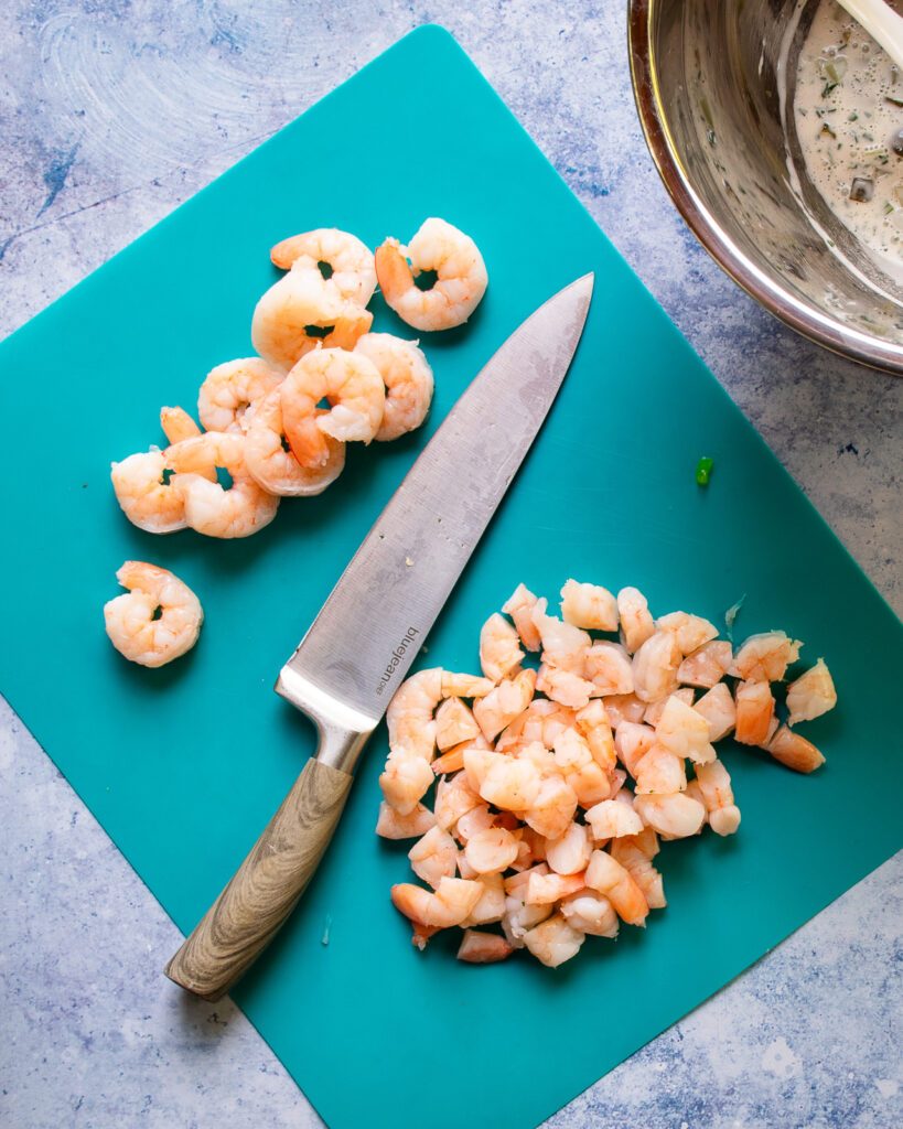 A turquoise chopping mat with a chef's knife and some shrimp in the process of being chopped.