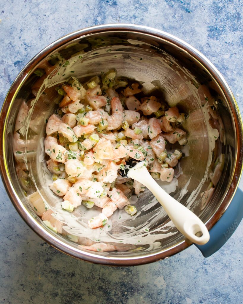 The filling for shrimp rolls mixed in a stainless steel bowl with a spatula sticking out of it.