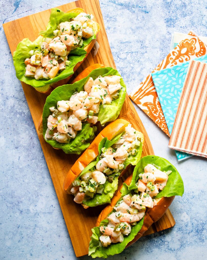 Four shrimp rolls on a wooden platter with some colorful napkins next to them.