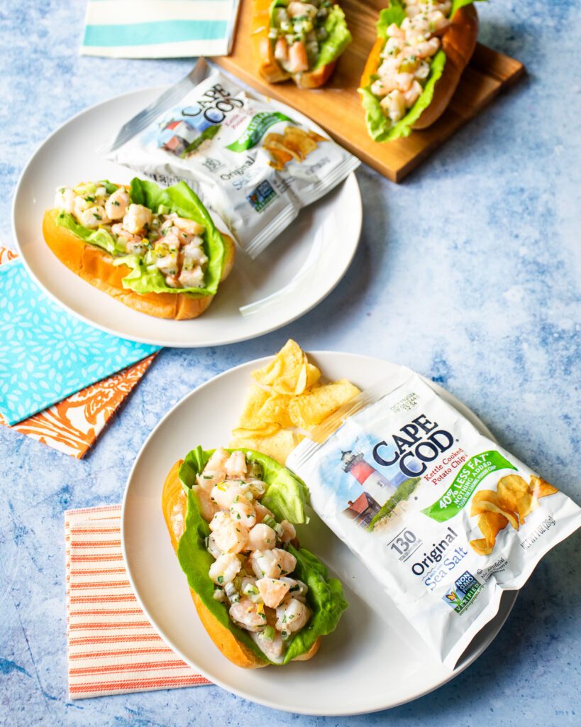 Two white plates with a shrimp roll and a small bag of chips on each one.