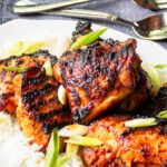 Korean grilled chicken on a platter of white rice with scallions scattered on top.