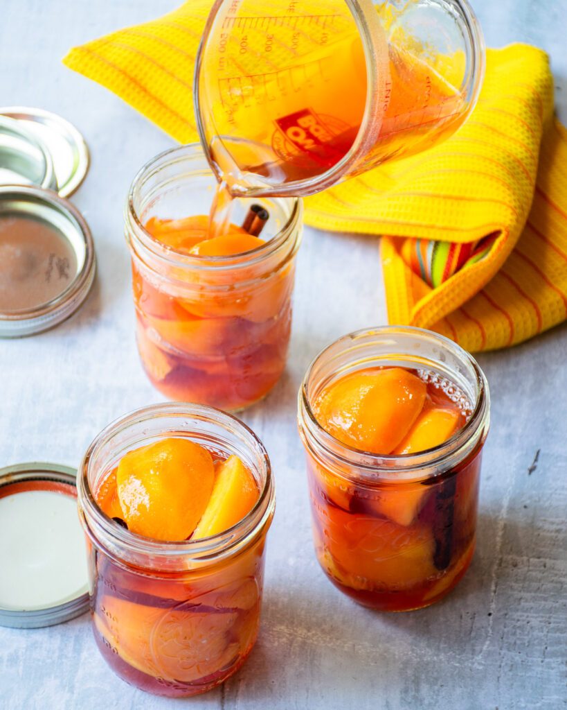 Three jars of pickled peaches being filled with pickling brine.