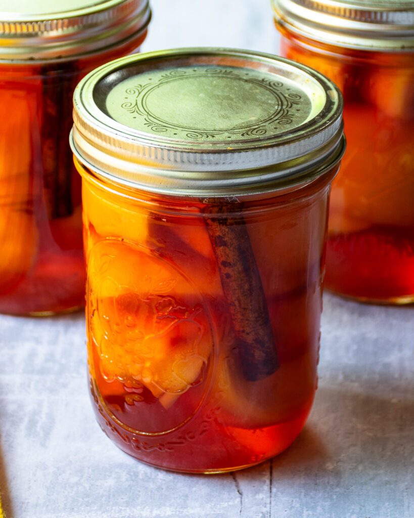 A jar of pickled peaches with two more in the background.