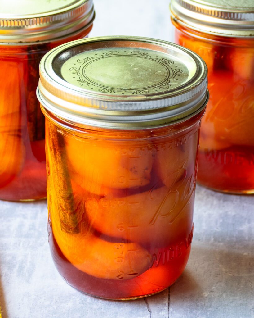 A jar of pickled peaches with two more in the background.