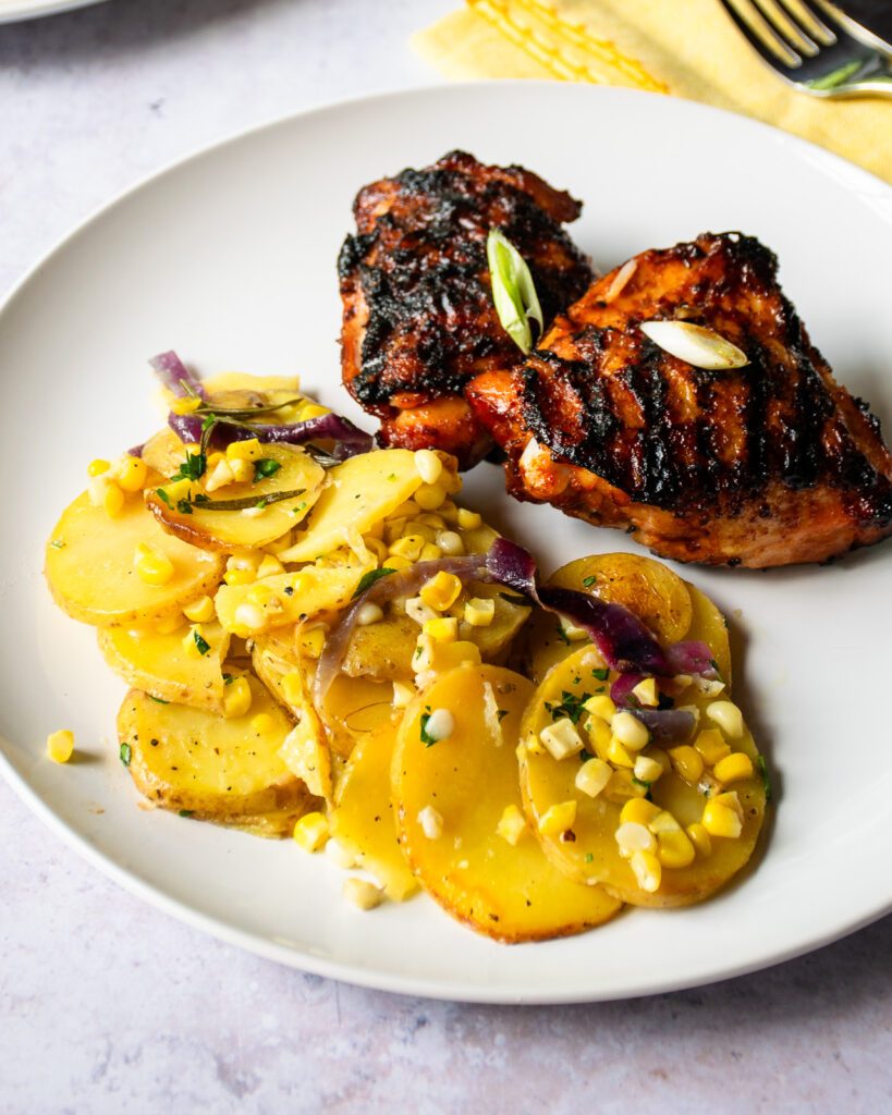 A white plate with foil packet vegetables and two grilled chicken thighs.