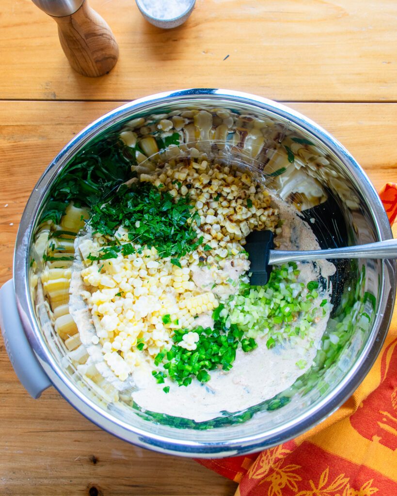 Looking down into a stainless steel bowl with the ingredients for corn dip in it. Salt and pepper near by and a spatula sticking out of the bowl.