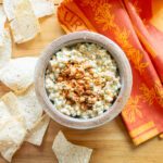 Looking down on a dish of corn dip with tortillas and an orange dish towel beside it.