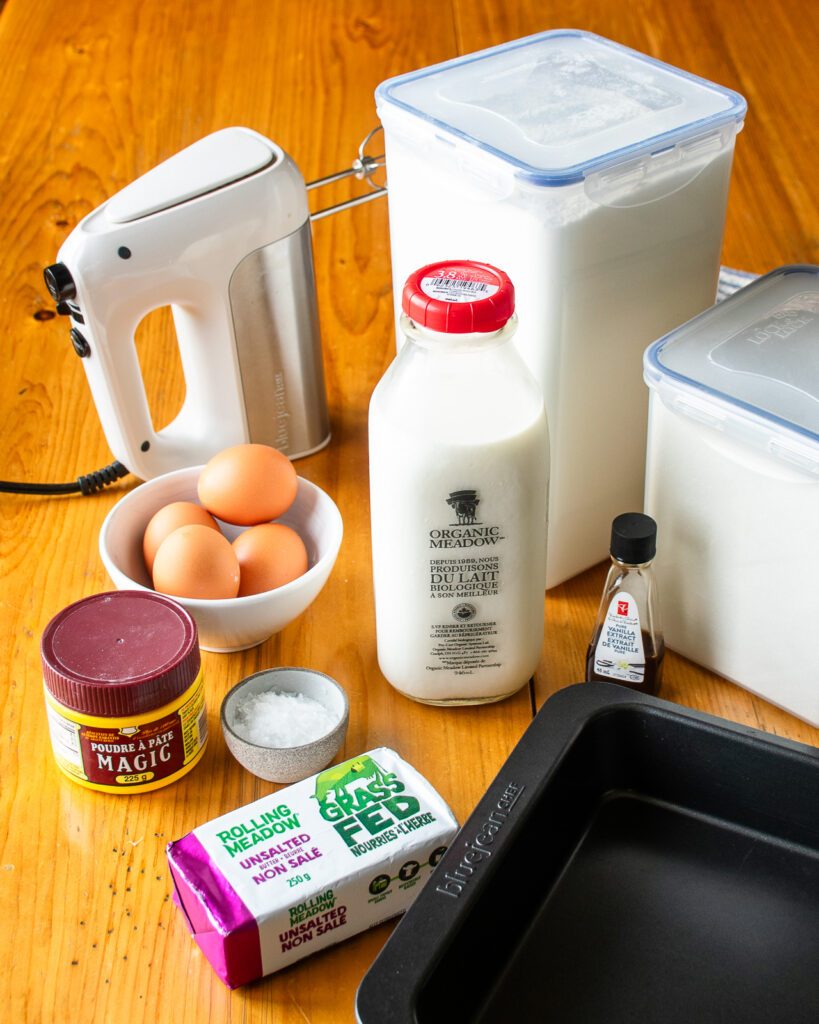 Ingredients on a wooden table - flour, sugar, butter, eggs, milk, baking powder, vanilla extract.