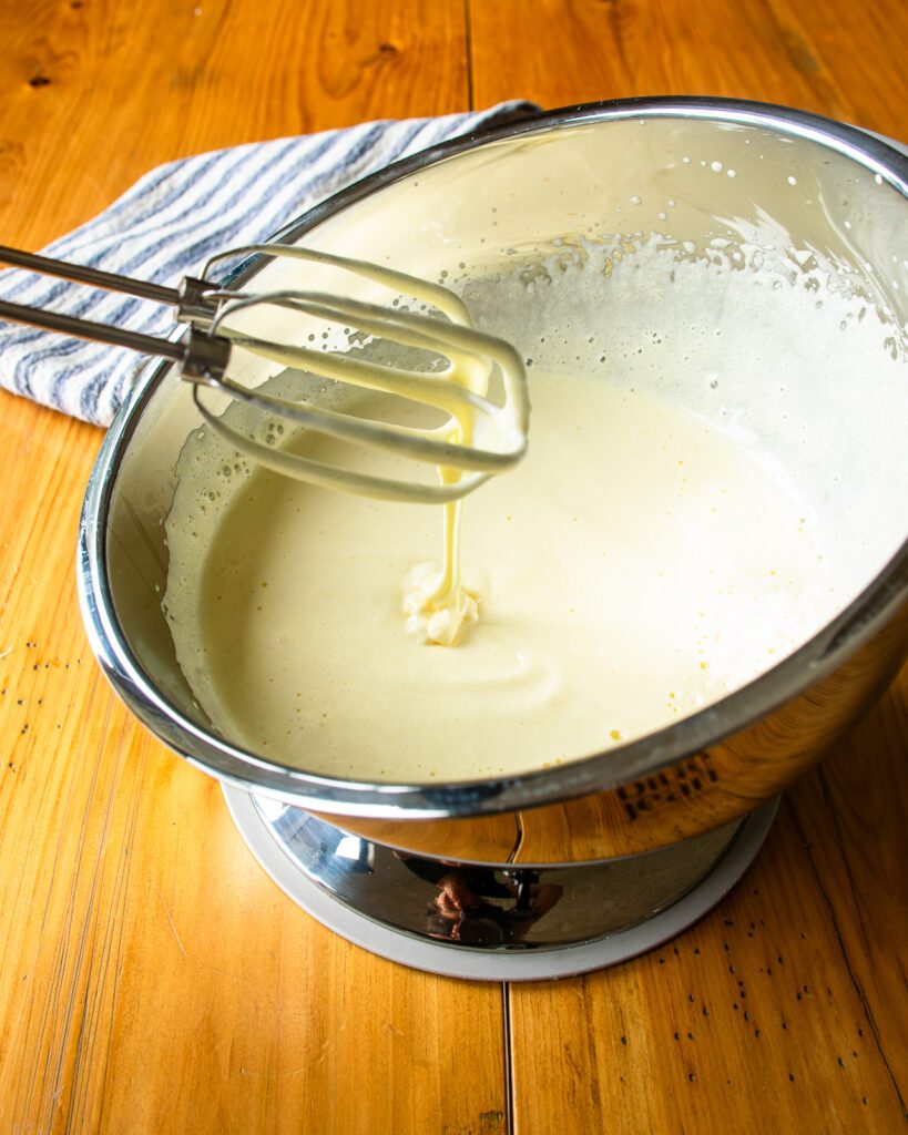 Beaters resting above whipped eggs and sugar in a stainless steel bowl.