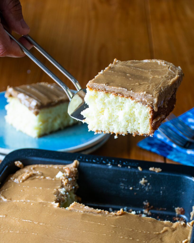 A spatula lifting a piece of hot milk cake from a cake pan.