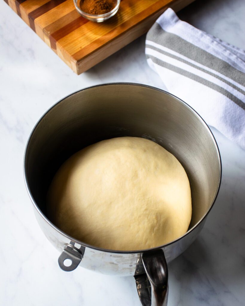 A ball of cinnamon roll dough in a stand mixer bowl.