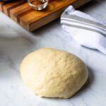 A ball of cinnamon roll dough on a countertop with some ingredients in the background.