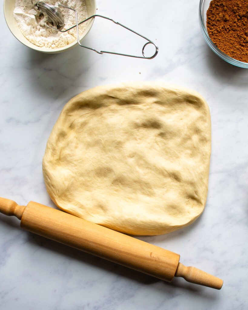 Cinnamon roll dough bing rolled out with a rolling pin, ingredients round.