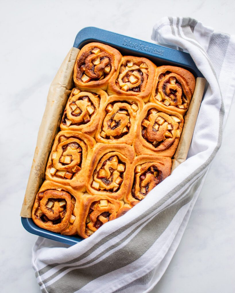 A blue baking pan with baked apple cinnamon rolls inside and a towel around two corners of the pan.