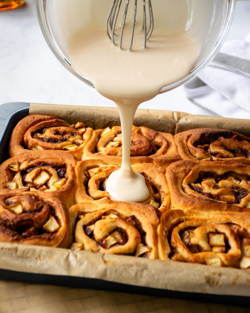 Maple icing being poured onto cinnamon rolls.