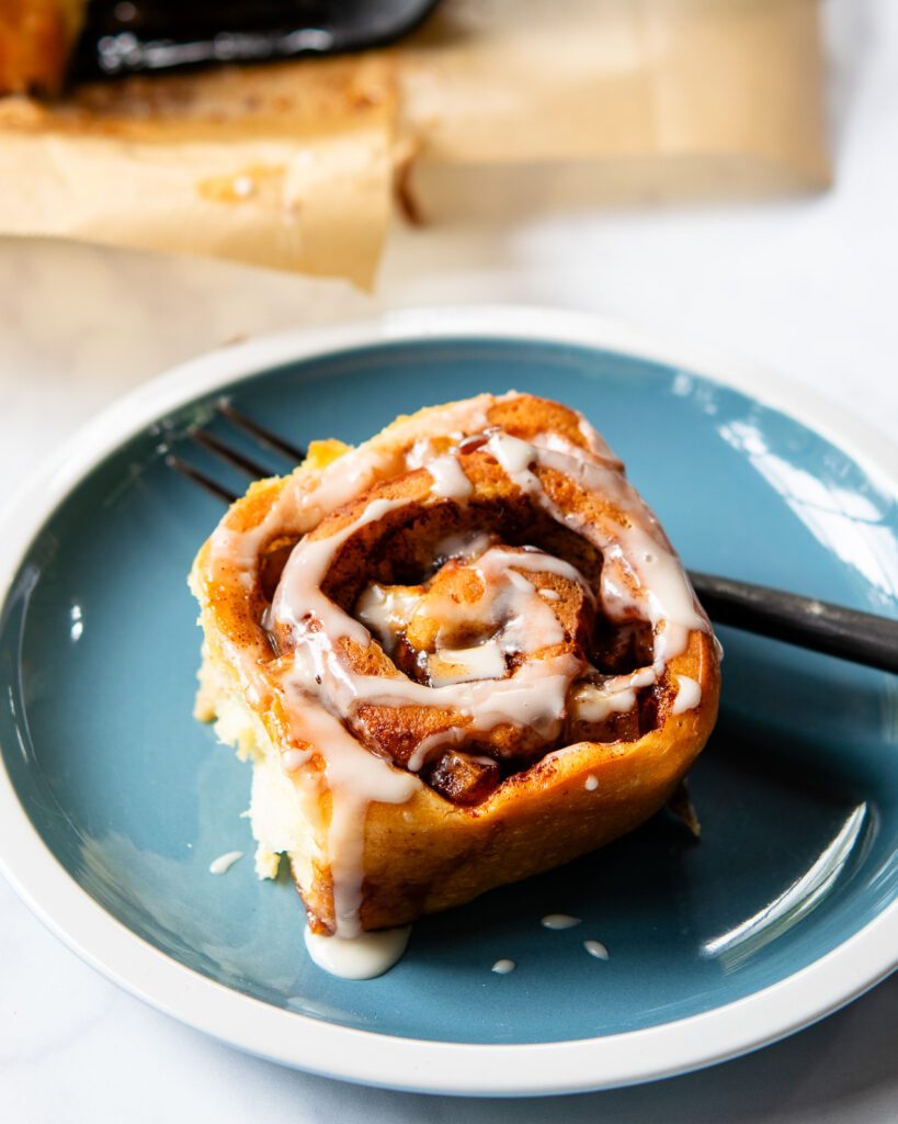 A single apple cinnamon roll on a blue plate with a fork.