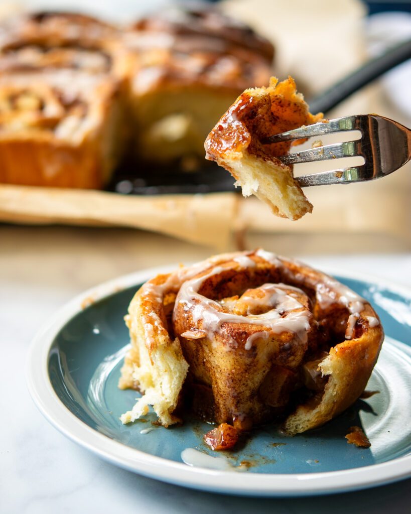 A fork lifting a piece of apple cinnamon roll from a plate.