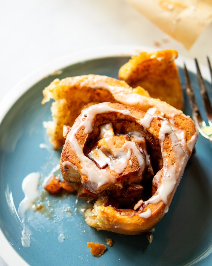 An apple cinnamon roll, partially eaten, on a blue plate.