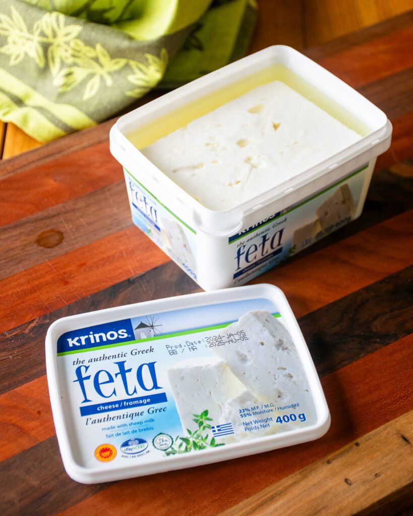 A tub of feta cheese open on a wooden cutting board.