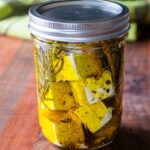 A pint jar with marinated feta inside and a green kitchen towel in the background.