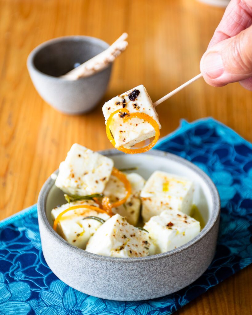 A toothpick picking up a piece of marinated feta cheese.