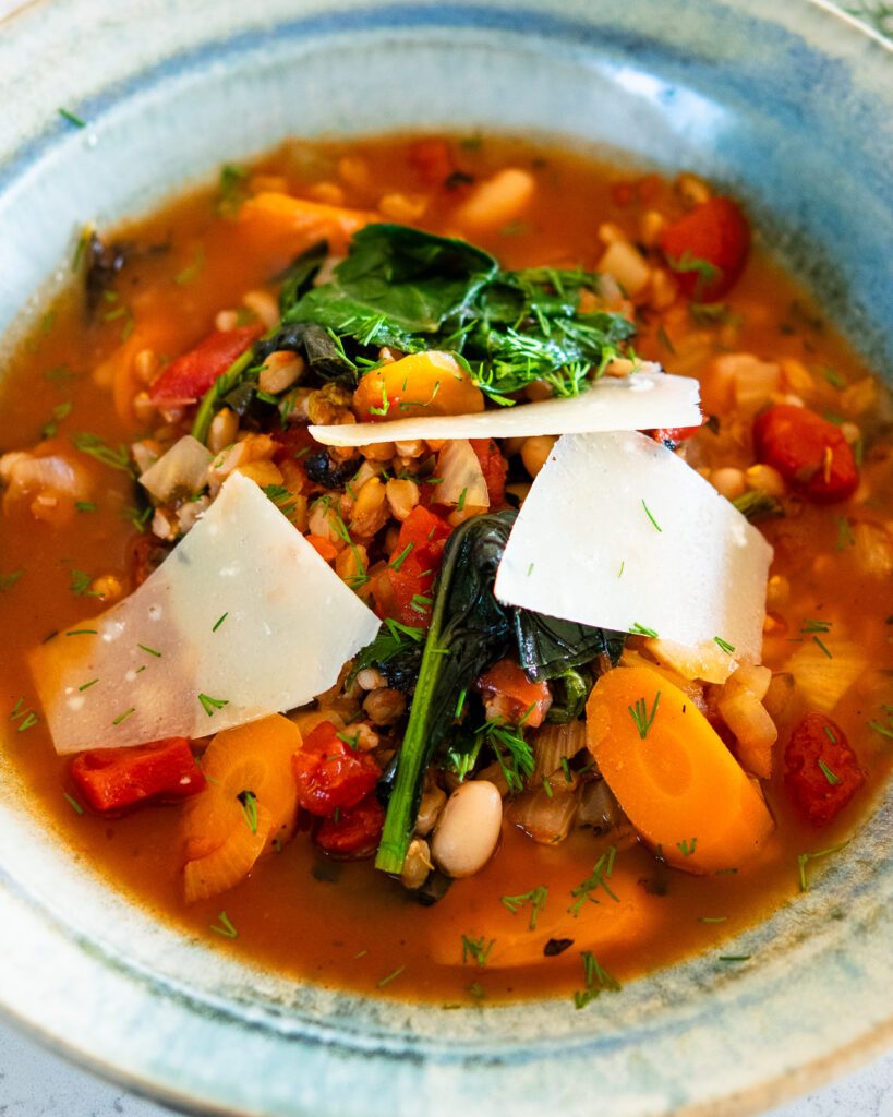 Tuscan Farro Soup in a pottery bowl with shards of parmesan cheese on top.