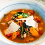 Tuscan Farro Soup in a pottery bowl with shards of parmesan cheese on top.