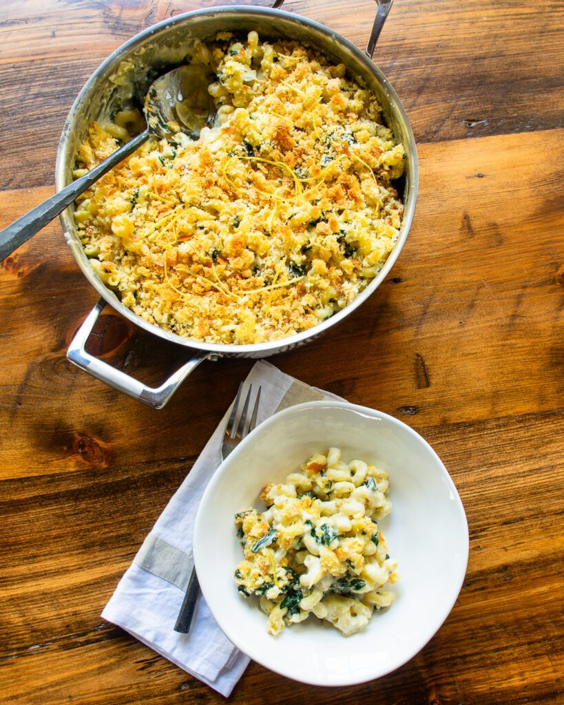 A saute pan and a white bowl both with spinach artichoke mac and cheese inside.