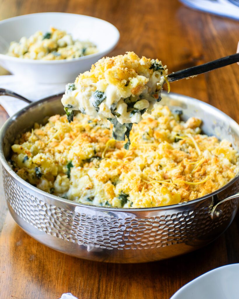 A spoon serving some spinach artichoke mac and cheese out of a saute pan.