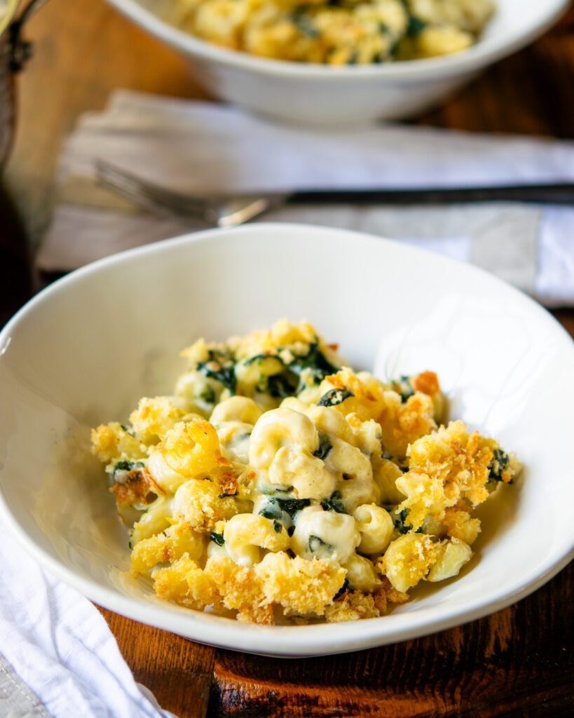 A white bowl with spinach artichoke mac and cheese inside.